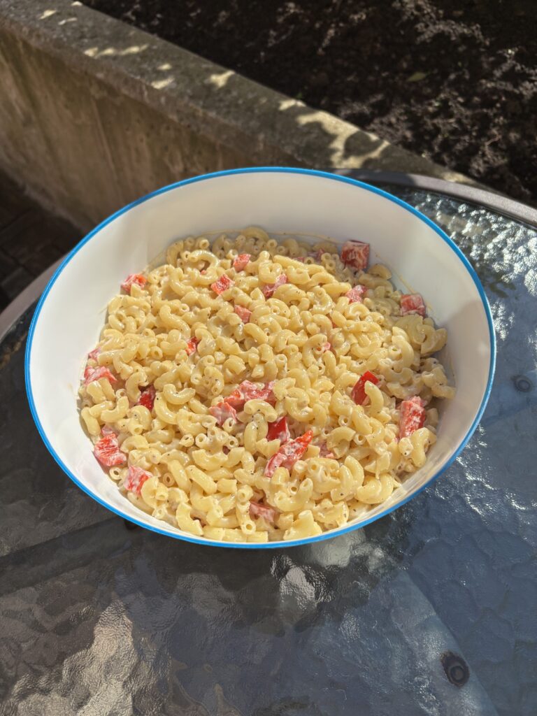 Macaroni salad in a blue bowl on a glass outdoor table