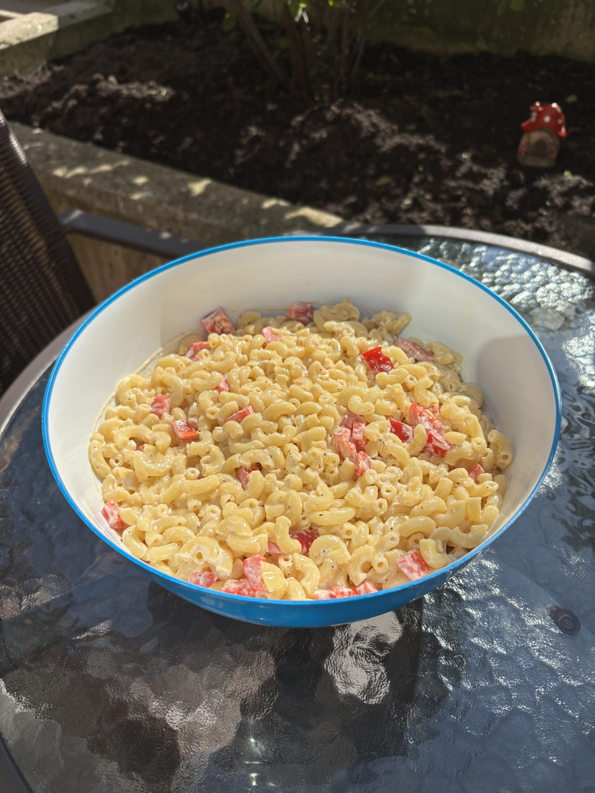 Macaroni salad in a blue bowl on a glass outdoor table