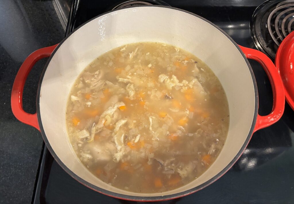 Chicken soup in a red dutch oven on a black stovetop