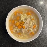 Chicken soup on a beige bowl on a black countertop
