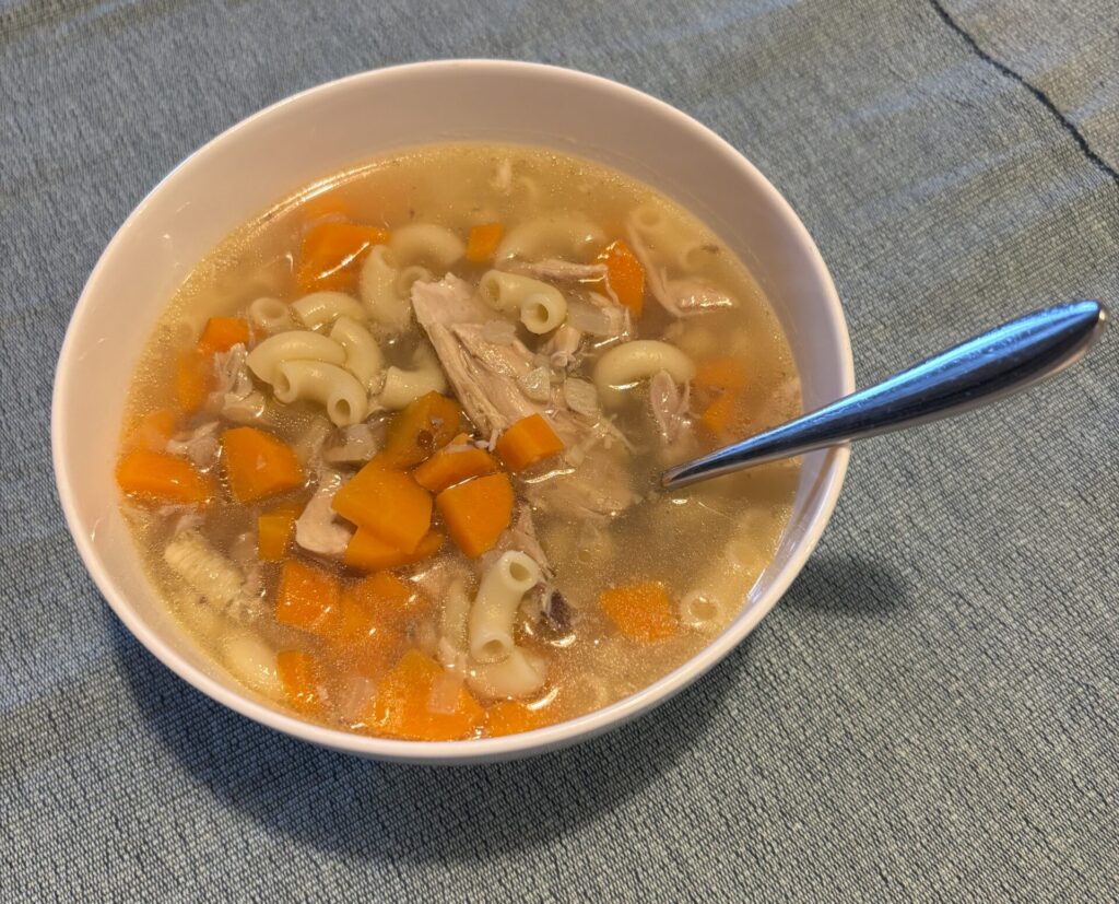 Chicken noodle soup in a beige bowl on a blue placemat