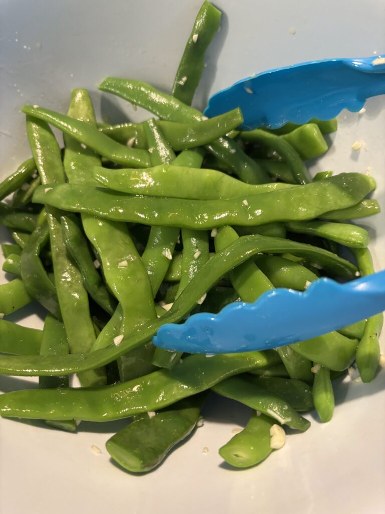 Garlic green beans in a bowl with blue tongs