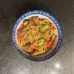 Chicken and vegetable stir-fried noodles in a blue and white bowl